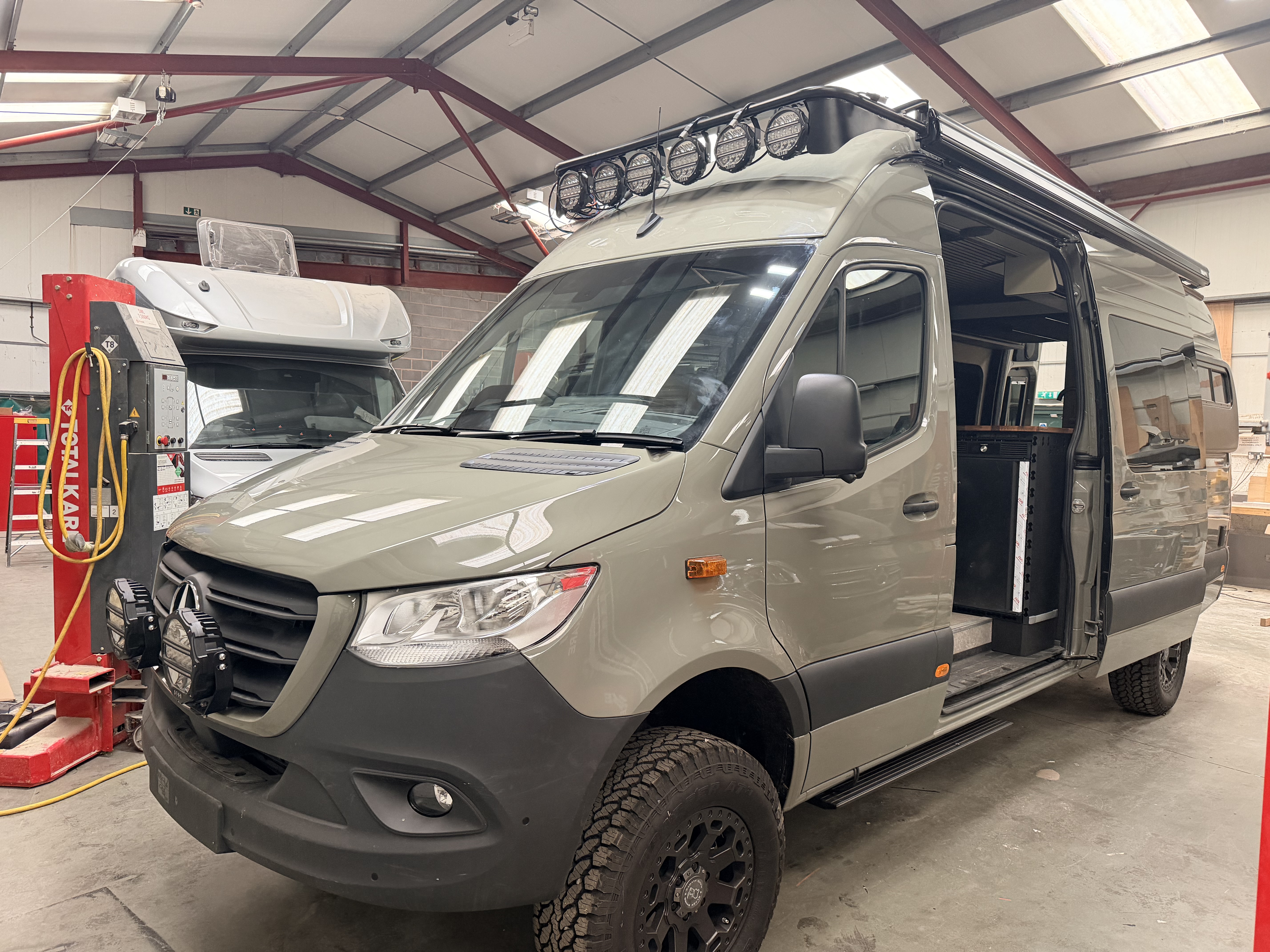 Greymatter 007 Iron Trail — moss grey AWD Mercedes Sprinter 4x4 in the Blackridge Overland workshop, roof rack and off-road tyres